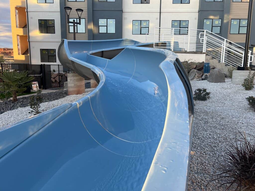 Curved blue slide outside modern building complex.