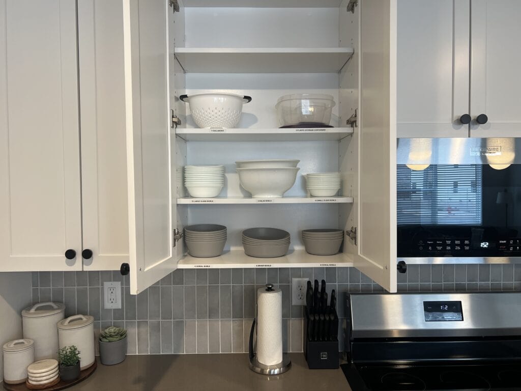 Open kitchen cabinet with bowls and colanders.