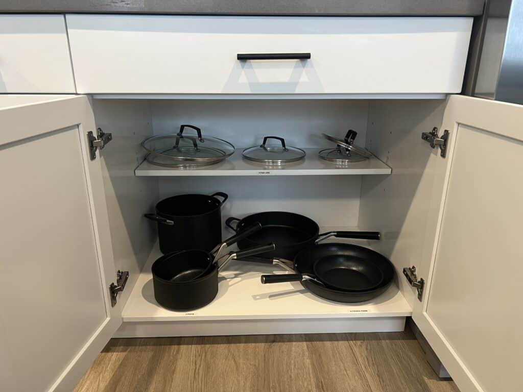 Kitchen cabinet with skillets and pots inside.