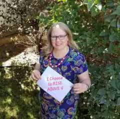 Woman holds motivational sign outdoors by greenery.