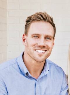 Smiling man in blue shirt against white brick wall.