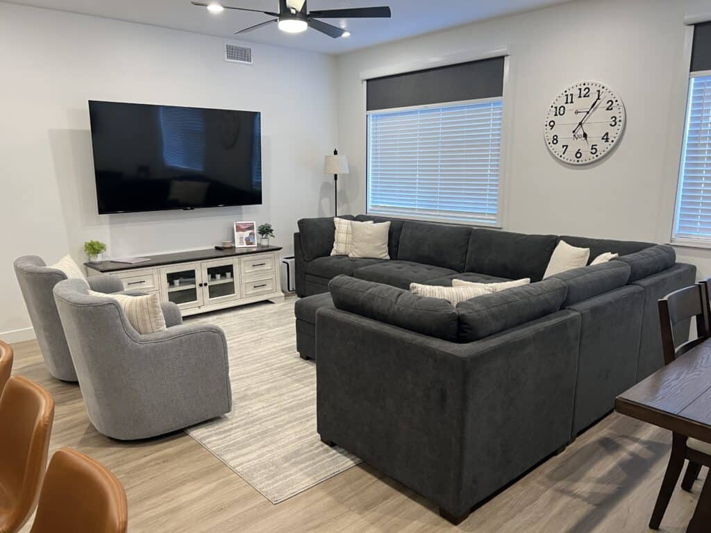 Modern living room with sectional sofa, TV, large clock.